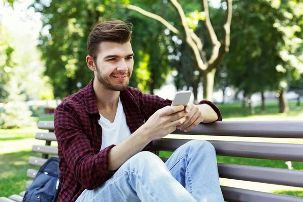 Bonito homem sentado e usando smartphone ao ar livre — Fotografia de Stock