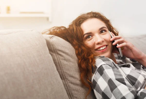 Boldog vöröshajú lány beszél a mobil kanapé — Stock Fotó