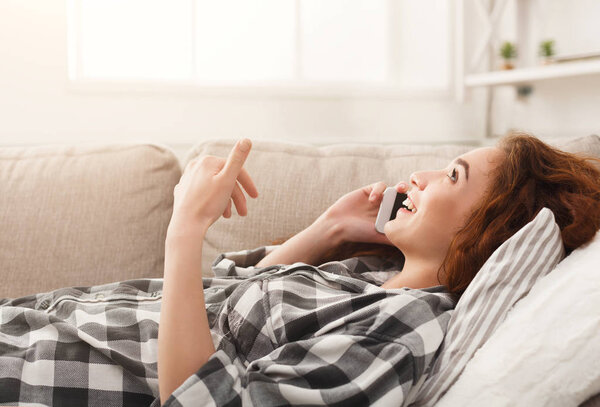 Young girl talking on mobile lying on beige couch