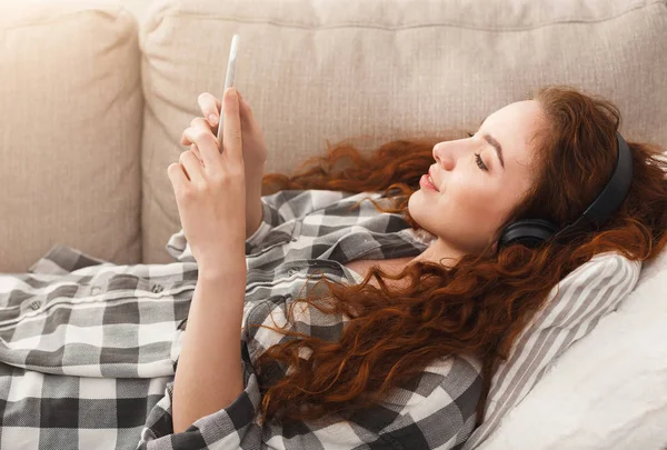 Jovem mulher em fones de ouvido no sofá bege — Fotografia de Stock