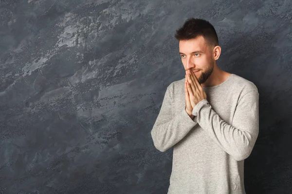 Bello giovane uomo che prega su sfondo grigio — Foto Stock