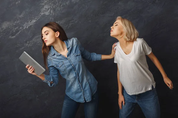 Curious female friends using tablet at dark studio background — Stock Photo, Image