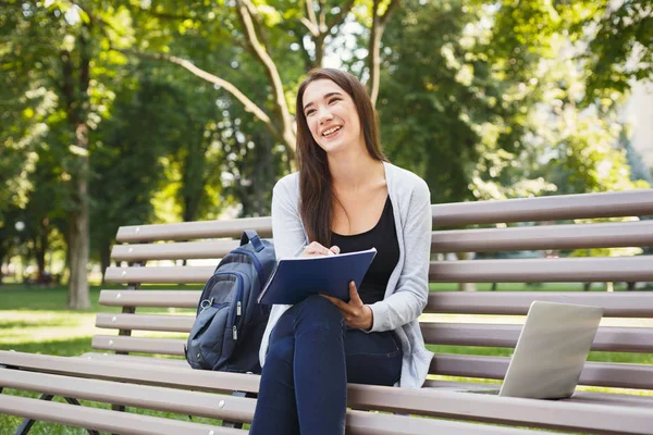Улыбающаяся студентка сидит в парке с ноутбуком — стоковое фото
