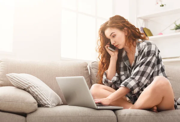 Meisje met laptop en mobiele zittend op beige Bank. — Stockfoto