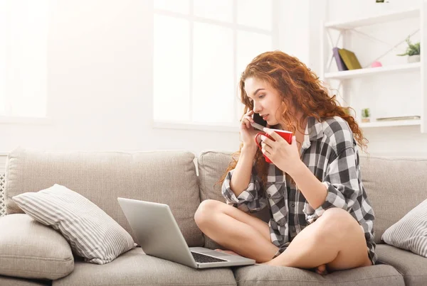 Menina com laptop e móvel sentado no sofá bege . — Fotografia de Stock