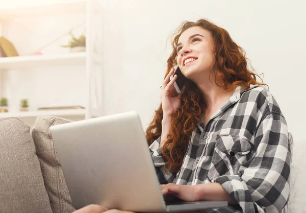 Meisje met laptop en mobiele zittend op beige Bank. — Stockfoto