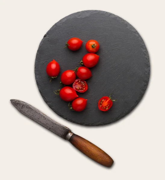 Rustic slate stone plate with tomatoes and knife, isolated over white background — Stock Photo, Image