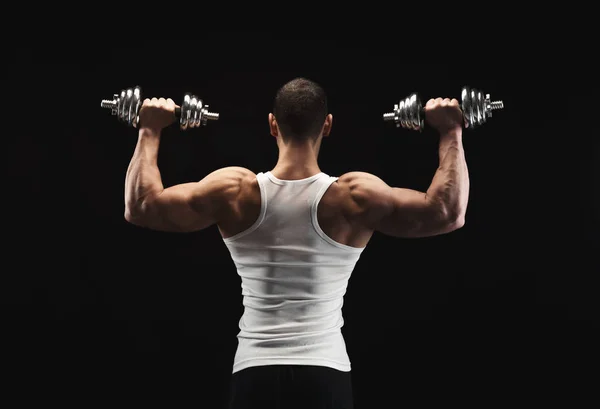 Сильный спортсмен с гантелями демонстрирует мускулистое тело — стоковое фото