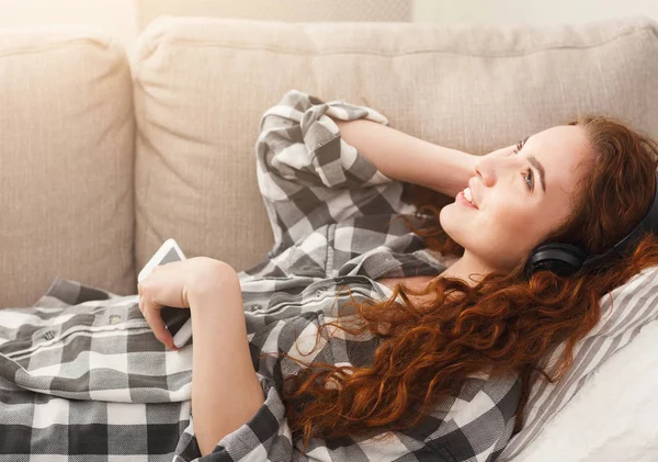 Молодая женщина в наушниках на бежевом диване — стоковое фото