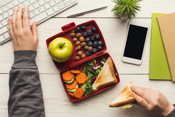 Женщина ест здоровый сэндвич из коробки с обедом за рабочим столом — стоковое фото