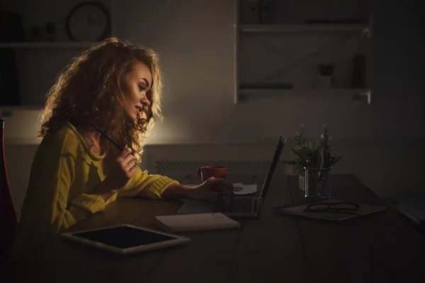 Donna sorridente che lavora con il computer portatile e prende appunti a casa — Foto Stock