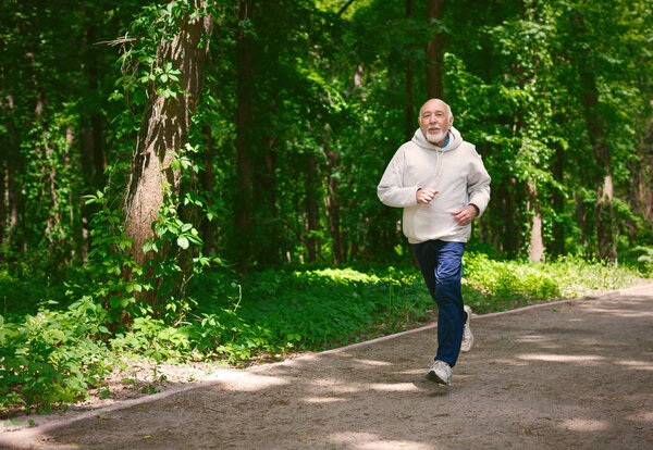 Elderly man running in green forest, copy space