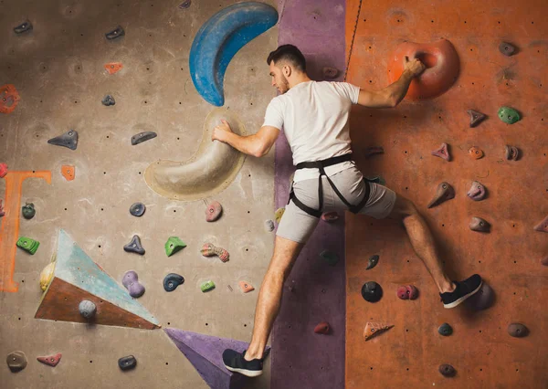 Young man climbing artificial rock wall at gym — Stock Photo, Image