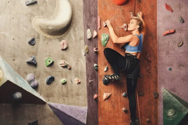 Young woman climbing artificial rock wall at gym — Stock Photo, Image