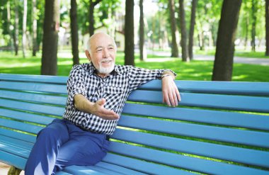 Parkta bankta oturan gülümseyen kıdemli adam