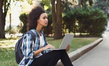 Dalgın öğrenci dizüstü kullanarak merdivenlerde oturan