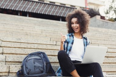 Gülümseyen öğrenci dizüstü kullanarak merdivenlerde oturan