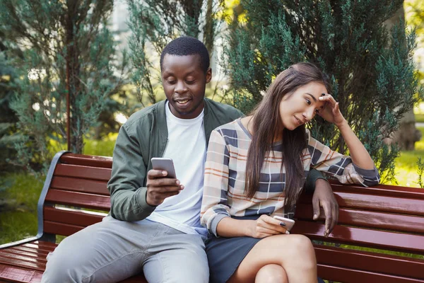Frau sitzt mit Mann im Park und nutzt Smartphone — Stockfoto