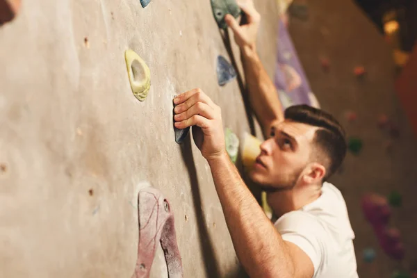 Jovem escalando parede de rocha artificial no ginásio — Fotografia de Stock