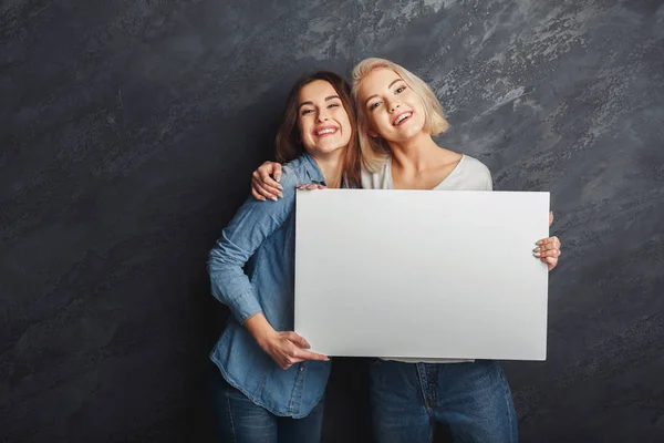 Filles heureuses avec bannière blanche vierge au fond sombre studio — Photo