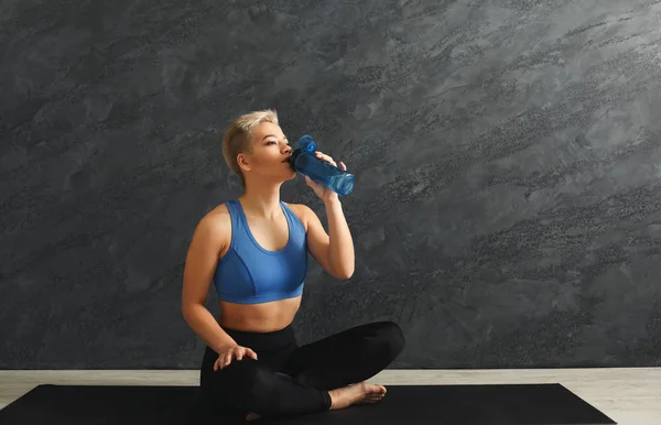 Fitness vrouw drinkwater op de sportschool op een grijze achtergrond — Stockfoto
