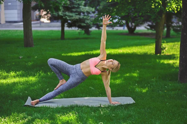 Woman training yoga in side plank pose outdoors