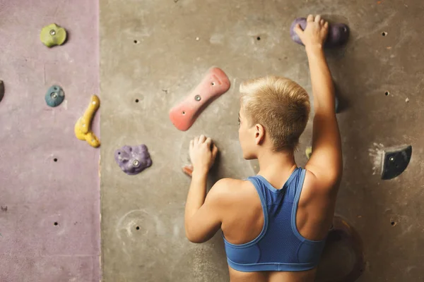 Молода жінка піднімається на штучну кам'яну стіну в спортзалі — стокове фото