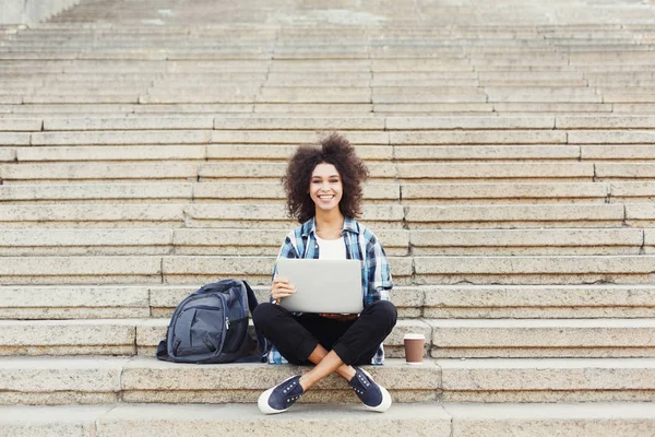Estudante sorrindo sentado nas escadas usando laptop — Fotografia de Stock
