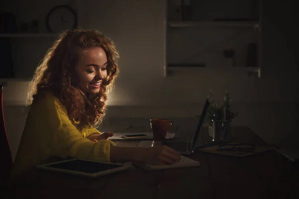 Donna sorridente prendere appunti a casa la sera — Foto Stock