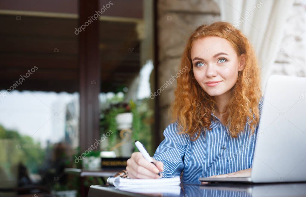 Young redhead girl making notes in a notebook