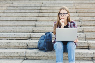 Dalgın öğrenci dizüstü kullanarak merdivenlerde oturan
