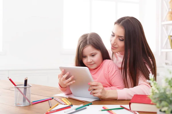 Lille pige og hendes mor ved hjælp af en tablet derhjemme - Stock-foto