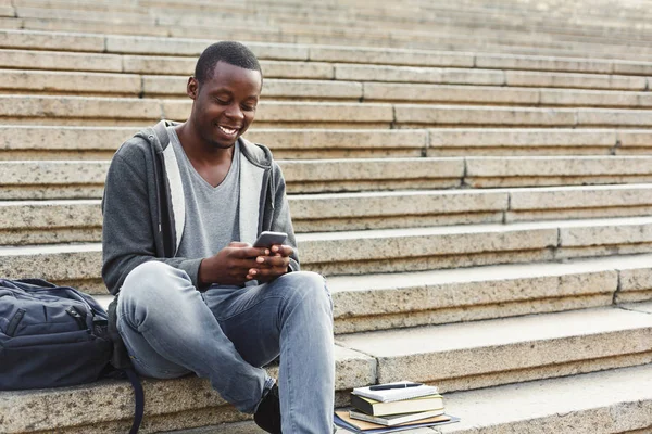 Estudante afro-americano feliz usando smartphone ao ar livre — Fotografia de Stock