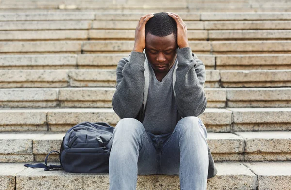 Estudante afro-americano desesperado sentado em escadas ao ar livre — Fotografia de Stock