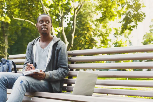 Joven estudiante afroamericano pensando con un libro de texto al aire libre —  Fotos de Stock