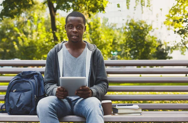 Smiling african-american student in the park with tablet oudoors