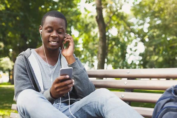 Estudante afro-americano sorridente ouvindo música ao ar livre — Fotografia de Stock