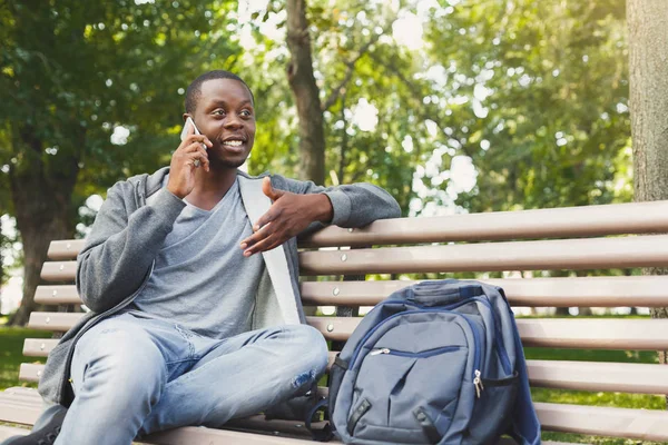 Estudante afro-americano sorrindo falando ao telefone ao ar livre — Fotografia de Stock