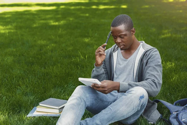 Συμπυκνωμένο Αφροαμερικανός studen κάθεται με το σημειωματάριο στο γρασίδι — Φωτογραφία Αρχείου