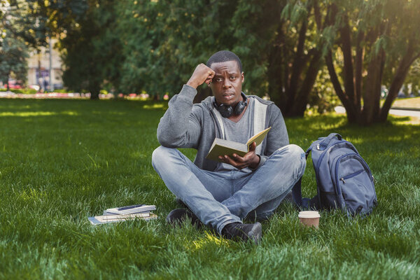 Отчаянная африканско-американская студентка читает книгу в кампусе на траве
