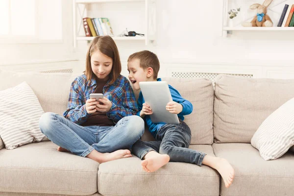 Twee kinderen met gadgets op de Bank thuis — Stockfoto