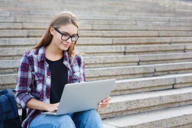 Gülümseyen öğrenci dizüstü kullanarak merdivenlerde oturan