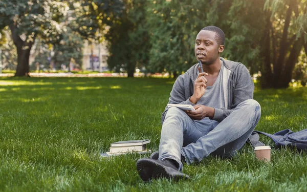 Konzentrierte afrikanisch-amerikanische Studentin sitzt mit Notizbuch im Gras — Stockfoto