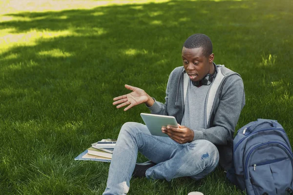 Verbaasd Afro-Amerikaanse student op gras met tablet oudoors — Stockfoto