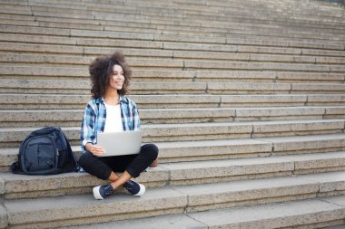 Gülümseyen öğrenci dizüstü kullanarak merdivenlerde oturan