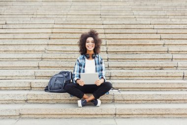 Gülümseyen öğrenci dizüstü kullanarak merdivenlerde oturan