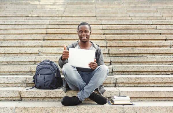 Lächelnder Student zeigt mit Laptop Daumen nach oben — Stockfoto