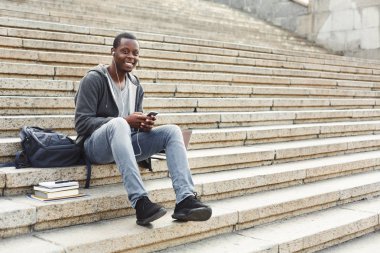 Merdivenlerde oturan ve onun smartphone açık havada kullanarak Afrikalı-Amerikalı öğrenci