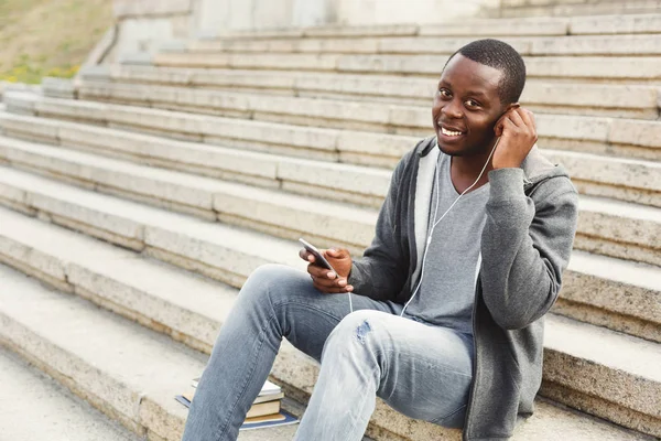 African-american student sitting on stairs and listening to music outdoors — Stock Photo, Image