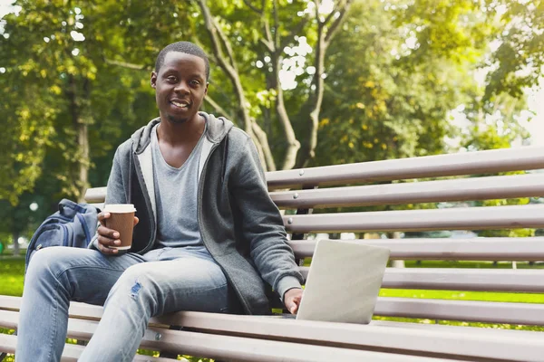 Αφρικανικός-Αμερικανός φοιτητής εργάζεται πάνω σε ένα φορητό υπολογιστή και πίνοντας τον καφέ έξω από — Φωτογραφία Αρχείου
